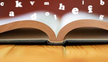 cerrar el libro de texto sobre una mesa de madera con alfabetos ingleses borrosos foto