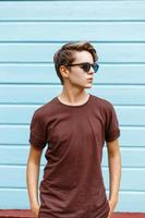 Handsome young guy with the hairstyle in sunglasses, t-shirt posing near a bright blue wooden wall photo