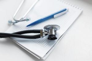 Phonendoscope with a pen and a notebook on a white table. The concept of insurance. photo