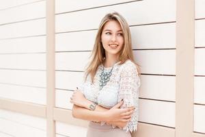 hermosa mujer con estilo sonriendo en una blusa de encaje y vestido se encuentra cerca de una pared de madera blanca. foto