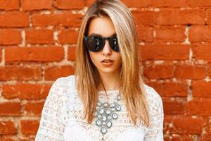 Portrait of a beautiful girl in a white lace shirt with sunglasses on a background of a brick wall photo