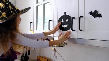 barn dekorerar de kök i Hem för halloween. flicka i en häxa kostym spelar med de dekor för de Semester - fladdermöss, domkraft lykta, pumpor. höst bekvämlighet i hus, scandi-stil kök, loft video