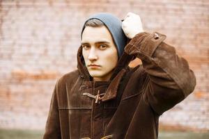 Young stylish man wears a hood on a background of red brick wall photo