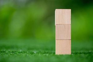 Stacking blank wooden cubes on green background with copy space for input wording and infographic icon. Empty brown wooden object block for symbol icon put technology, zero gravity, business concept. photo