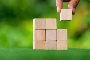 Stacking blank wooden cubes on green background with copy space for input wording and infographic icon. Empty brown wooden object block for symbol icon put technology, zero gravity, business concept. photo