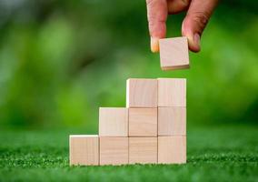 Stacking blank wooden cubes on green background with copy space for input wording and infographic icon. Empty brown wooden object block for symbol icon put technology, zero gravity, business concept. photo