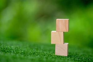 Stacking blank wooden cubes on green background with copy space for input wording and infographic icon. Empty brown wooden object block for symbol icon put technology, zero gravity, business concept. photo