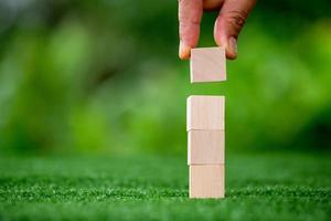 Stacking blank wooden cubes on green background with copy space for input wording and infographic icon. Empty brown wooden object block for symbol icon put technology, zero gravity, business concept. photo