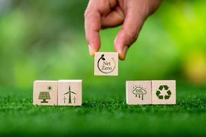 Net zero and carbon neutral concept. Net zero greenhouse gas emissions target. Climate neutral long term strategy. Wooden cubes with green net zero icon and green conserve icon on nature background. photo