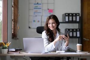 Young woman working on a laptop in the office. Asian businesswoman sitting at her workplace in the office. Beautiful Freelancer Woman working online at her home. photo