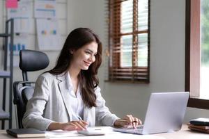 Young woman working on a laptop in the office. Asian businesswoman sitting at her workplace in the office. Beautiful Freelancer Woman working online at her home. photo