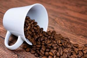 Black coffee foil packaging bag on wooden table top view. Spilled beans flat lay concept. Room for text. photo