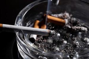 Ashtray and smoking cigarette on black background photo