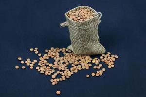 brown dried lentils in a burlap bag on black background photo