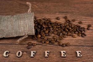 Black coffee foil packaging bag on wooden table top view. Spilled beans flat lay concept. Room for text. photo