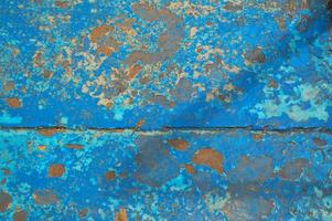 The texture of the iron metal painted blue paint old battered scratched cracked ancient rusty metal sheet wall with corrosion. The background photo