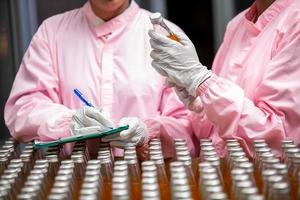 Asian woman worker with clipboard is checking product bottles of fruit juice on the production line in the beverage factory. Manufacturer checks quality of food industry. photo