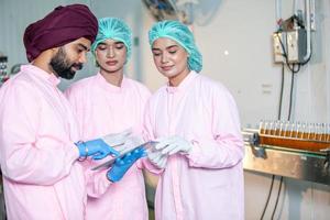 Group of Asian worker with clipboard is checking product bottles of fruit juice on the production line in the beverage factory. Manufacturer checks quality of food industry. photo