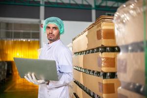 trabajador con computadora portátil está revisando el producto en la línea de producción en la fábrica de bebidas. el fabricante comprueba la calidad de la industria alimentaria. foto