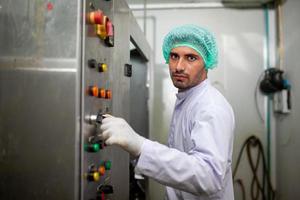 el trabajador controla la máquina operativa y enciende el interruptor en la línea de producción en la fábrica de bebidas. foto