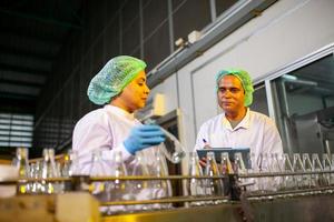 Asian workers with clipboard is checking product bottles of fruit juice on the production line in the beverage factory. Manufacturer checks quality of food industry. photo