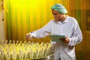 trabajadores asiáticos con portapapeles están revisando botellas de jugo de frutas en la línea de producción en la fábrica de bebidas. el fabricante comprueba la calidad de la industria alimentaria. foto