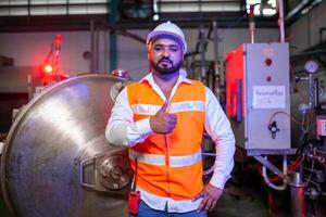 Professional engineer with helmet works to maintain industrial construction equipment. Worker is standing in the factory with thump up. photo