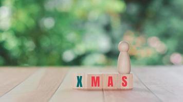 concepto del día de navidad. una figura humana de madera se alza sobre un bloque de madera con texto xmas. foto