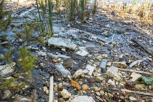 montones de residuos de construcción, residuos domésticos, espuma y botellas de plástico en la orilla de un lago forestal, problemas de contaminación ambiental foto