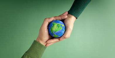 World Earth Day Concept. Green Energy, ESG, Renewable and Sustainable Resources. Environmental Care. Hands of People  Embracing a Handmade Globe. Protecting Planet Together. Top View photo