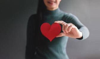 Love, Health Care, Donation and Charity Concept. Close up of Smiling Volunteer Woman Holding a Heart Shape Paper. presenting to Camera photo