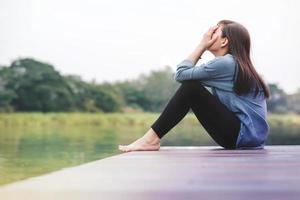 concepto de mal día. tristeza mujer sentada junto al río en la terraza de madera del patio. sin rostro con cuerpo completo, vista lateral foto