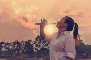 mujer joven asiática bebiendo agua después de trotar, foto