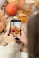 Girl taking photo of pumpkins, autumn leaves and teapot on a window. Girl photographing on phone rustic halloween composition. Happy Thanksgiving and Halloween