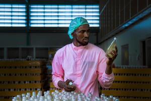 trabajador científico en una fábrica de bebidas embotelladas con sombrero de seguridad posando para comprobar la calidad de los productos de semillas de albahaca en la cinta transportadora antes de su distribución al negocio del mercado. foto