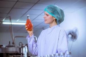 Worker of science in bottle beverage factory wearing safety hat posing show work to check quality of Basil seed produce on conveyer belt before distribution to market business. photo