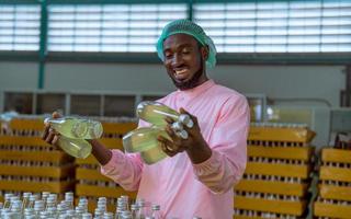 Worker of science in bottle beverage factory wearing safety hat posing show work to check quality of Basil seed produce on conveyer belt before distribution to market business. photo