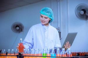 Worker of science in bottle beverage factory wearing safety hat posing show work to check quality of Basil seed produce on conveyer belt before distribution to market business. photo