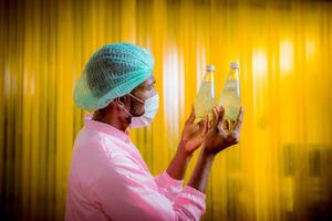 Worker of science in bottle beverage factory wearing safety hat posing show work to check quality of Basil seed produce on conveyer belt before distribution to market business. photo