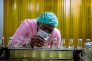 Worker of science in bottle beverage factory wearing safety hat posing show work to check quality of Basil seed produce on conveyer belt before distribution to market business. photo