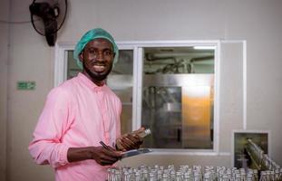 Worker of science in bottle beverage factory wearing safety hat posing show work to check quality of Basil seed produce on conveyer belt before distribution to market business. photo