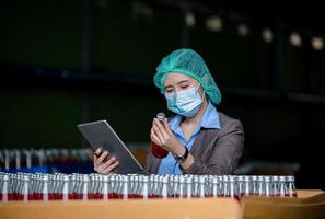 Worker of science in bottle beverage factory wearing safety hat posing show work to check quality of Basil seed produce on conveyer belt before distribution to market business. photo