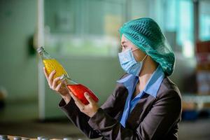 Worker of science in bottle beverage factory wearing safety hat posing show work to check quality of Basil seed produce on conveyer belt before distribution to market business. photo