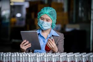 Worker of science in bottle beverage factory wearing safety hat posing show work to check quality of Basil seed produce on conveyer belt before distribution to market business. photo