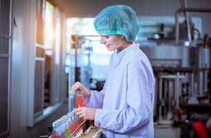 Worker of science in bottle beverage factory wearing safety hat posing show work to check quality of Basil seed produce on conveyer belt before distribution to market business. photo