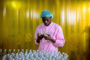 Worker of science in bottle beverage factory wearing safety hat posing show work to check quality of Basil seed produce on conveyer belt before distribution to market business. photo