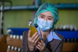 Worker of science in bottle beverage factory wearing safety hat posing show work to check quality of Basil seed produce on conveyer belt before distribution to market business. photo