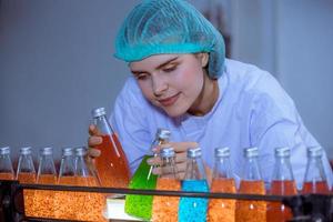 Worker of science in bottle beverage factory wearing safety hat posing show work to check quality of Basil seed produce on conveyer belt before distribution to market business. photo