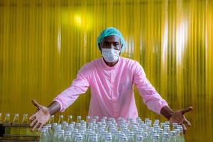 Worker of science in bottle beverage factory wearing safety hat posing show work to check quality of Basil seed produce on conveyer belt before distribution to market business. photo
