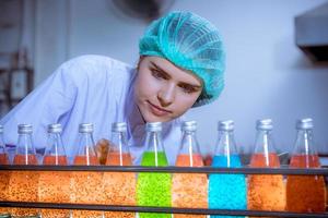 Worker of science in bottle beverage factory wearing safety hat posing show work to check quality of Basil seed produce on conveyer belt before distribution to market business. photo